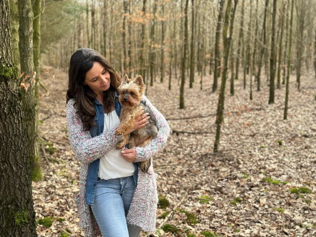 Yvonne Gröger mit ihrem kleinen Hund auf dem Arm in einem lichten Wald