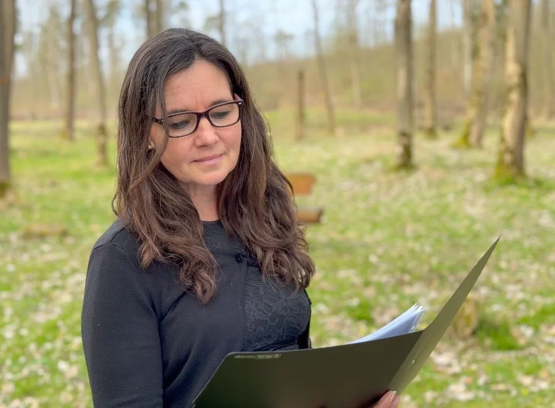 Yvonne Gröger blickt in eine Mappe mit ihrer Rede, im Hintergrund Wald