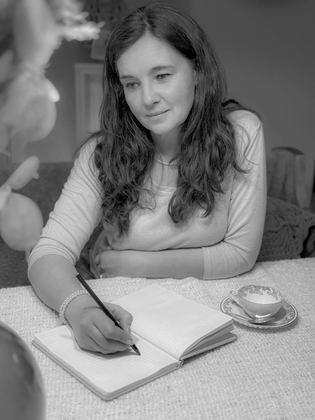Yvonne Gröger in Schwarzweiß beim Schreiben in ein Notizbuch, daneben eine Tasse Kaffee